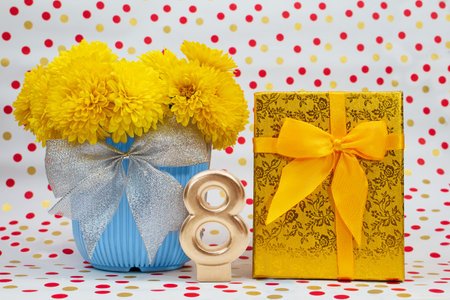 Bouquet of yellow chrysanthemums in blue pot with bow and golden gift box, number 8, behind white background with polka dots. International Women's Day, March 8, birthdayの写真素材