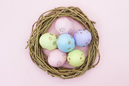 Painted multicolored eggs in wooden nest of branches on pink background. view from above. Easter,...
