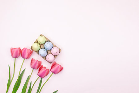 Pink tulips with basket of colored eggs in corner with place for text. Easter. pastel background. copy spaceの写真素材