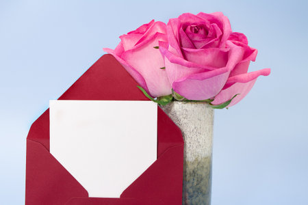 Red envelope with place of paper for text and vase of pink roses on blue background. Invitation, birthday, March 8, International women's, mother's day. copy spaceの写真素材