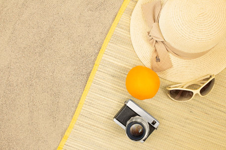 Straw hat with orange, sunglasses, camera on sunbed on beach sand. rest, travel. vertical and horizontal. copy spaceの写真素材