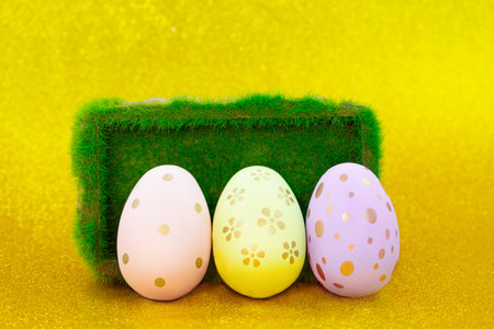 Painted eggs with pedestal with grass on yellow shiny background. Easter. copy spaceの写真素材