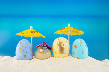 happy easter. Yellow and blue eggs with puffer fish under umbrellas on sandy beach of sea or ocean. Holiday postcard in hot country. Travel, spring, summer. copy spaceの写真素材