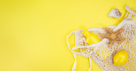 Starfish, shells with bag string with sunscreen bottle mockup and lemon from the side on yellow background. Concept of summer time, vacation, travel. Banner. copy spaceの写真素材