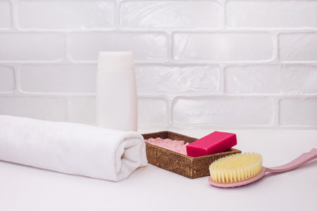 Towel, bottle mockup, body brush, pink soap, sea salt on white bathroom background. Concept of self care, bath, spa. copy spaceの写真素材
