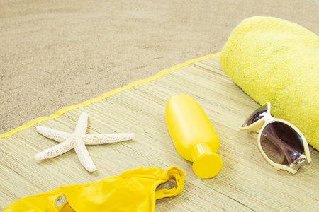 Starfish, yellow swimsuit and towel with glasses, bottle of sunscreen on straw lounger on beach background. vacation, travel conceptの写真素材