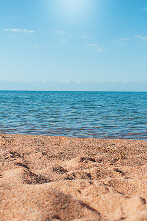 Beach with uneven sand and sea. Sun is shining, behind mountains. vertical. Leisure, travel, vacation. copy spaceの写真素材