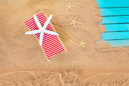 Star fish on striped red white lounge chairs on sandy beach with wooden board on coast with sea,...