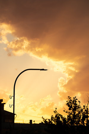 Sunset or dawn sky, yellow clouds with rays and hidden sun with black roof silhouette, lantern. Verical. copy spaceの写真素材