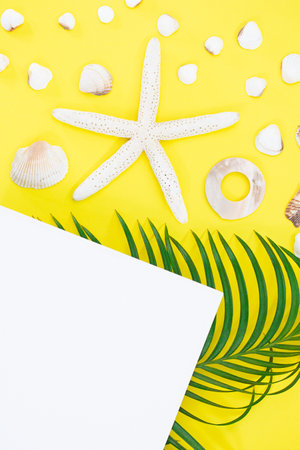 White starfish, shells with palm leaves and paper for text on side on yellow background. flat lay. Travel, vacation, summer. copy spaceの写真素材