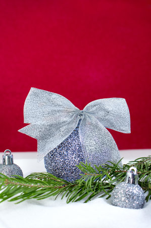 Silver Christmas balls with glitter bow and fir branch in snow on red background. Happy New Year card. Copy spaceの写真素材