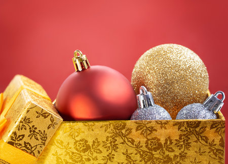 Christmas red, gold, silver balls in open yellow box on red background. New Year decor. Copy spaceの写真素材