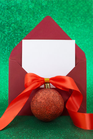 Christmas blank greeting card mockup with red glitter ball with bow and ribbon on sparkling green background. Envelope with letter with white paper. Vertical. Copy spaceの写真素材