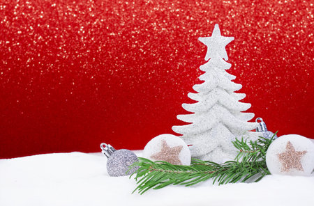 White shiny Christmas tree with silver balls and stars with pine branch on snow on side, behind sparkle red background. New Year. Copy spaceの写真素材