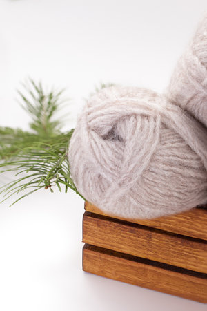 Gray wool skeins or yarn in brown box with spruce branch on white background. Handmade, knitting, hobby. Copy spaceの写真素材