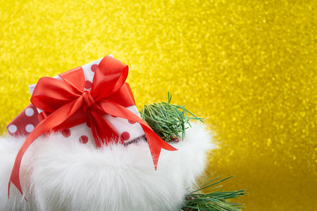Open fluffy bag with gift box with polka dot and red bow and fir branches on yellow blurred background with soft focus. Christmas, New year, birthday, sale, black Friday. Copy spaceの写真素材