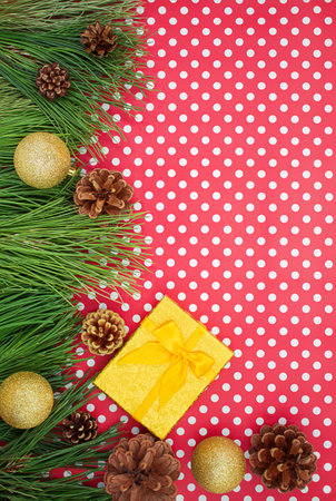 Golden yellow gift box with bow, fir branches with pine cones and shiny balls on red white with polka dot background. Christmas, New year, birthday. Copy spaceの写真素材