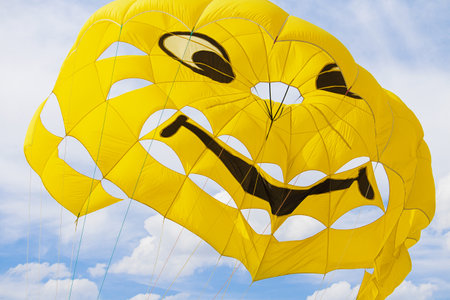 Bright yellow parachute with smile on sky with clouds background. Concept of extreme sport, adventure, challenge, relaxationの写真素材