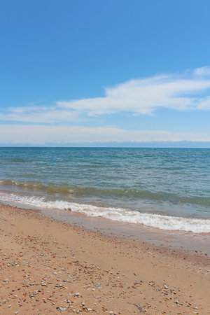 Beach with wave and wet sand with pebble on blue sky and mountains. Sea, ocean background. Vacation outdoor and travel holiday adventure concept. Verticalの写真素材