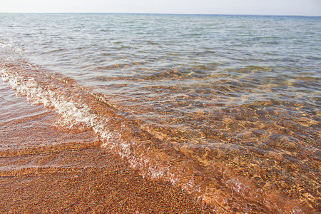 Orange yellow sand and pebbles seashore with wave on sunny day on sea. Vacation, travel, landscape. Copy spaceの写真素材