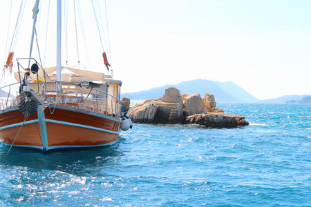 Yacht with folded sail with white and brown sloop is anchored to rock in open sea on clear sunny day. Deck on bow, mast and sails in calm seaの写真素材