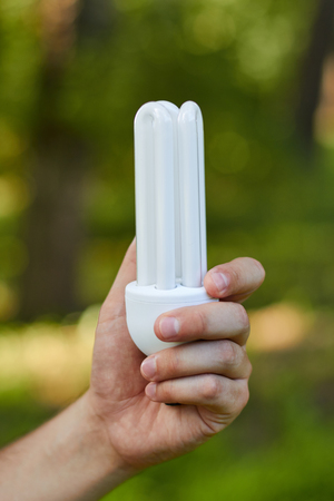 Hand holding compact  fluorescent lamp in hand, over grass backgroundの写真素材