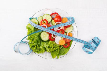 Plate with fresh vegetables salad and measured tape isolated on whiteの写真素材