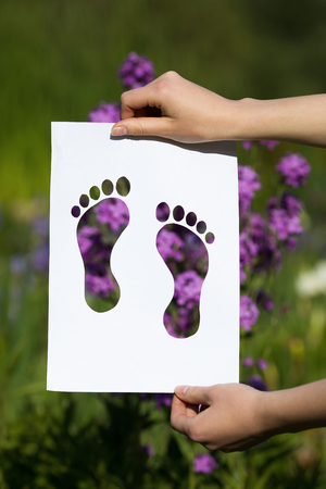 Hands holding papercut of miniature toe heels over blooming flowersの写真素材