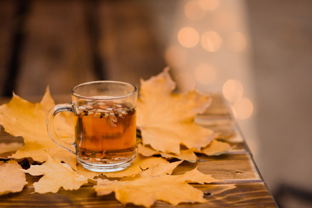 a cup of tea and yellow leaves on a wooden tableの写真素材