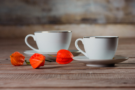 two white cups and flowers physalis on a wooden backgroundの写真素材