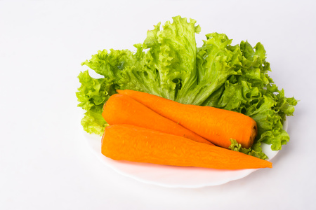 3 carrots and lettuce leaves on a white plate and on a white backgroundの写真素材