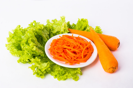 two carrots, sliced carrots on a white plate and lettuce leaves on a white backgroundの写真素材
