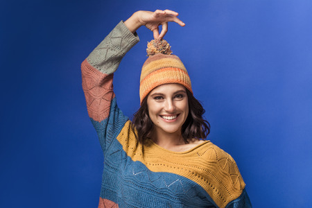 smiling girl in knitted sweater and yellow hat on blue background