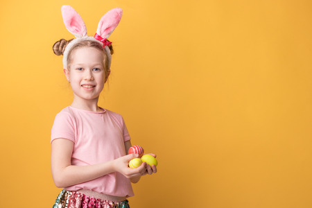 girl with bunny ears holds painted Easter eggs on a yellow background