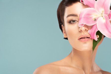 beautiful brunette with a short haircut and a pink lily on a blue backgroundの写真素材