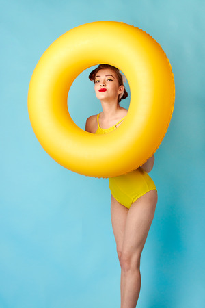 blonde in a bathing suit and with an inflatable circle on a blue backgroundの写真素材