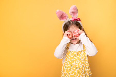 little girl with ears of a hare holds painted eggs on a yellow background