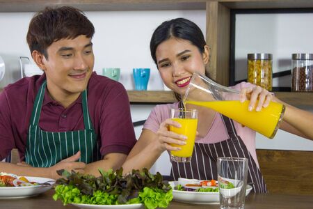Asian couple having breakfast together while wife is pouring orange juice for husband in kitchen roomの写真素材