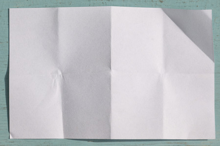 Page of White paper folded and wrinkled on blue wooden background with shadowの写真素材
