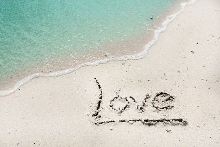 Word Love handwritten on sandy beach with soft ocean wave on backgroundの写真素材