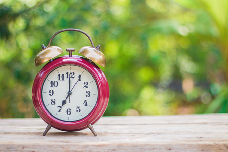 An antique red alarm clock on a wooden floor with a green background in the morning.の写真素材
