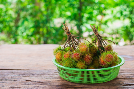 Rambutan from the garden put into a container. Placed on a wooden table with a green background.の写真素材