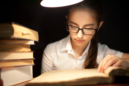 Young girl reading book under lamp in the darkの写真素材