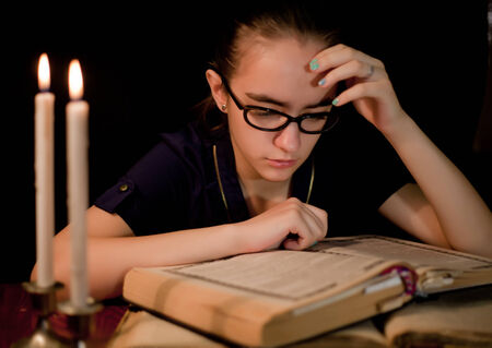 Girl reading book in dark library with candlesの写真素材