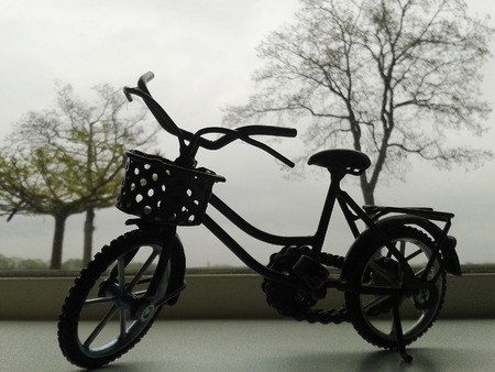 A little black bike model by the window with dry trees on the backgroundの写真素材
