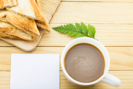 Coffee mug with green foot fern, baked bread and notes on yellow rustic table.の写真素材