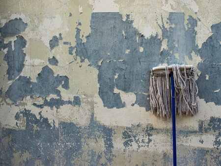 An old concrete wall with paint cracks and peeling off and a mop laid on its side.の写真素材