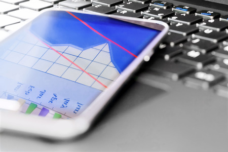 Smartphone on laptop keyboard with business graph reflectionの写真素材