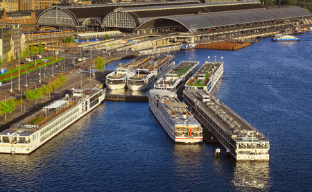 Amsterdam, Netherlands - MAY 12, 2016: River cruise terminal with ships and Centraal Train Station in Amsterdam in the morningのeditorial素材