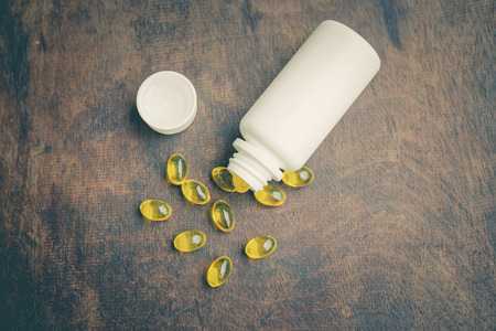 Fish oil capsule with pill bottle on wooden table. Health care and medical concept.の写真素材